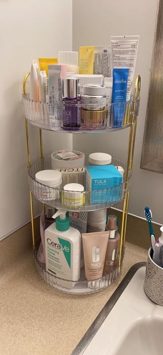 A three-tiered bathroom rack holding a variety of skincare products and toiletries.