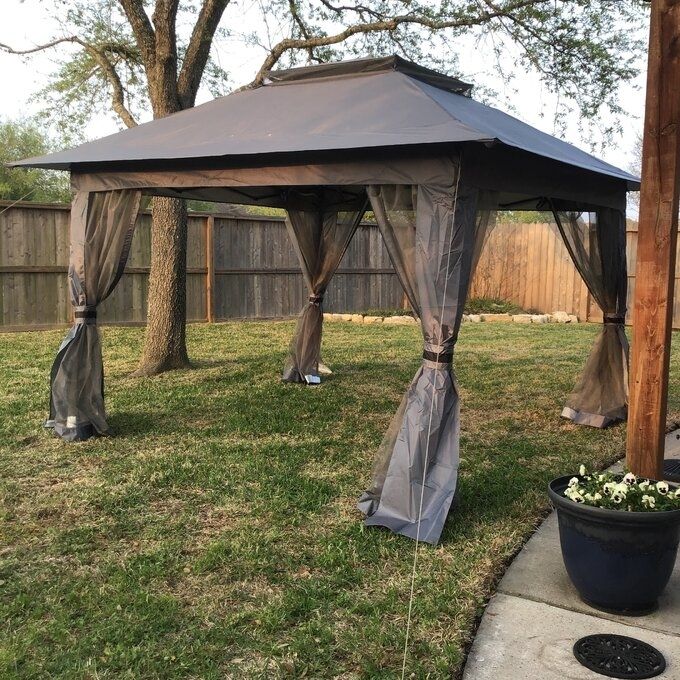 A gazebo with retractable mesh curtains, set up in a backyard and ideal for outdoor décor