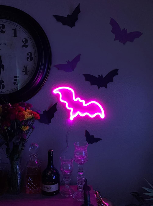 the neon pink bat sign on a reviewer's wall alongside paper black bats