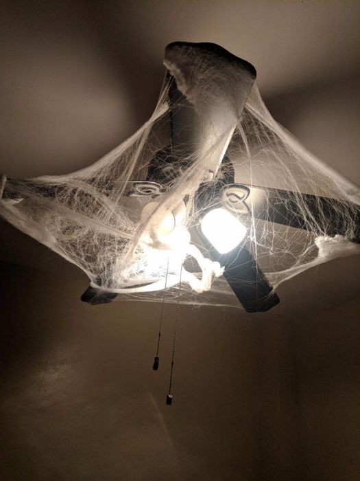 the spider webbing draped around an indoor ceiling fan and lamp