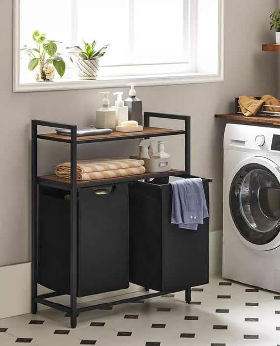 A laundry room setup featuring a washing machine, a shelving unit stacked with towels and storage containers, plus two black bins for extra organization.