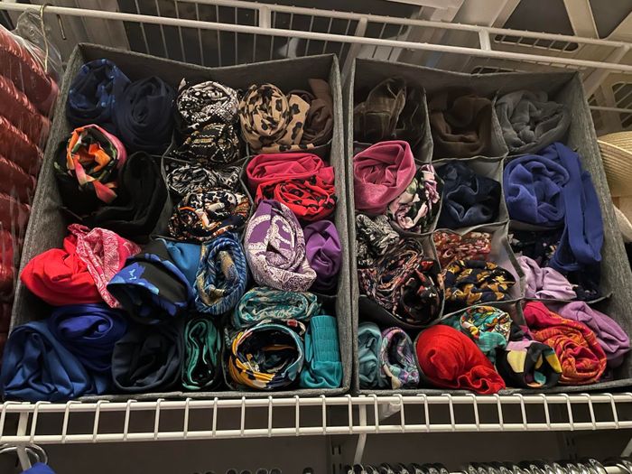 A shelf with gray storage bins holding an assortment of patterned and solid-colored fabrics