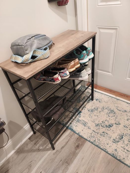 A compact shoe rack holding several pairs of shoes and hats, neatly arranged in an entryway atop a patterned rug