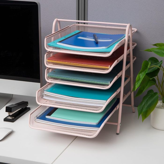 A five-tier desk organizer filled with colorful folders on a workspace next to a computer, a plant, and office supplies