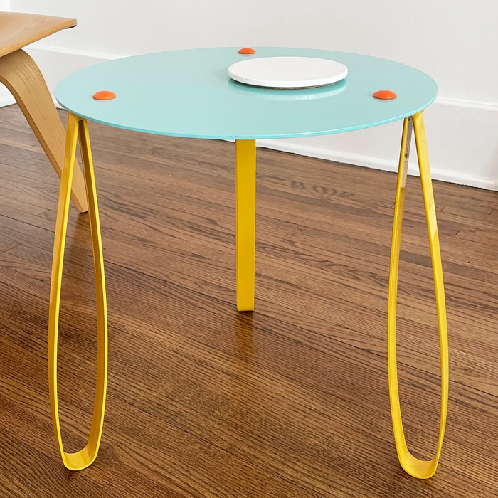 The yellow, teal, and orange table, topped with a simple white coaster.