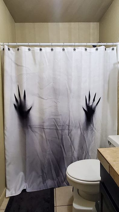 Reviewer's bathroom is shown with spider shower hooks holding up a spooky shower curtain