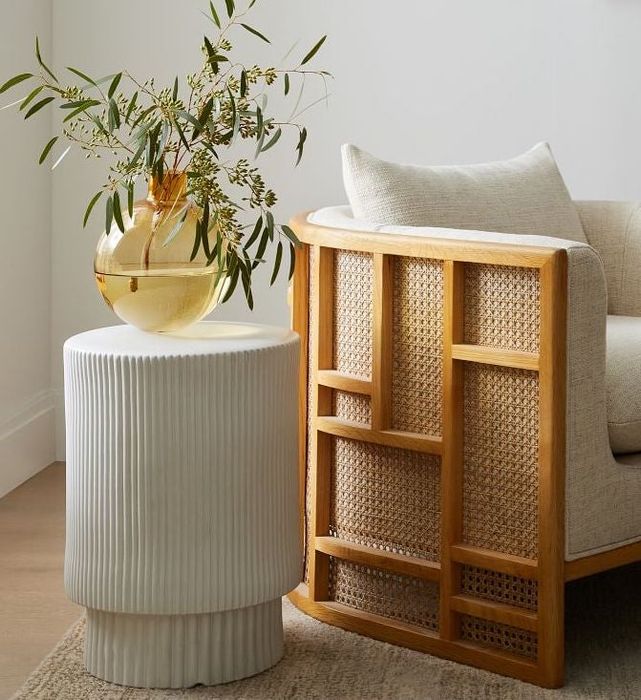 The white side table with a yellow vase placed next to a rattan armchair.