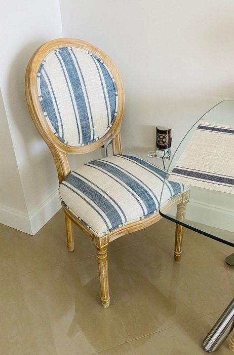 A close-up of a Louis XVI-style dining chair with striped blue and white upholstery