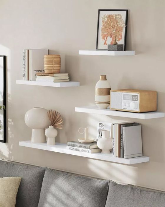 Three floating shelves mounted on a wall, featuring decorative items like books, vases, a radio, and framed artwork.