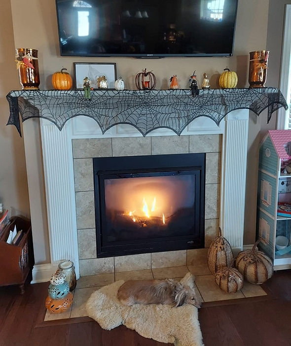 the black spiderweb mantel scarf draped over a fireplace, adorned with Halloween decorations on top