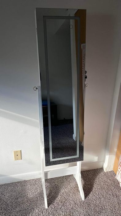 A full-length mirror jewelry cabinet with a lock and key, positioned against a wall