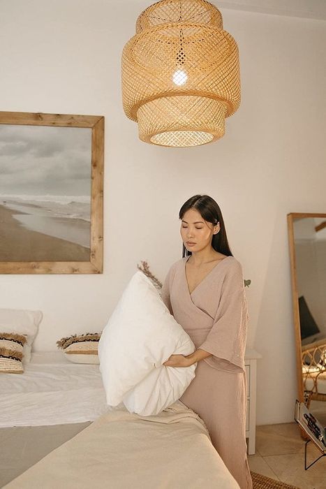 A three-tiered woven pendant light crafted from rattan, with a person tidying their bed beneath it