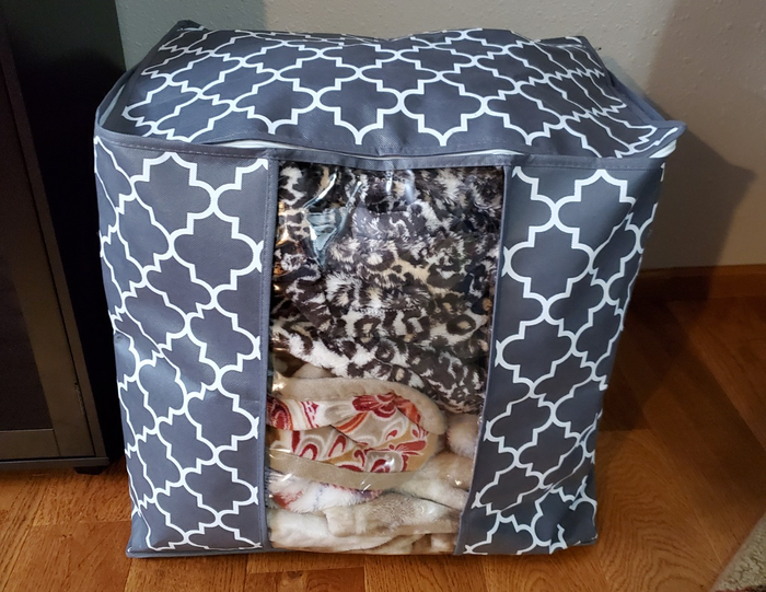 A storage bag with folded blankets clearly visible through its transparent front panel