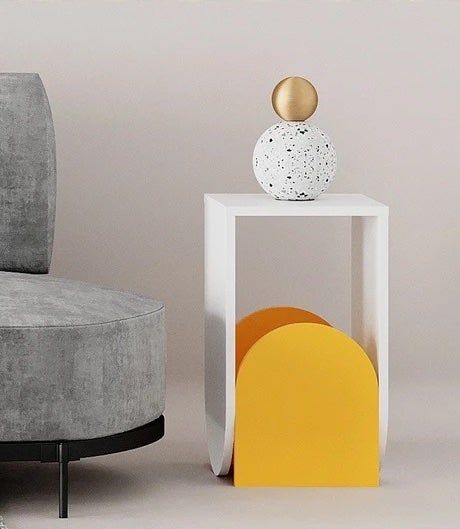 The yellow and white side table beside a gray couch, holding a spherical sculpture.