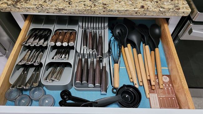 A reviewer demonstrates an organized kitchen drawer featuring three gray silverware organizers.