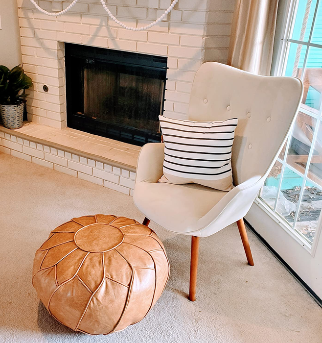 a reviewer photo of the tan pouf placed in front of a white chair
