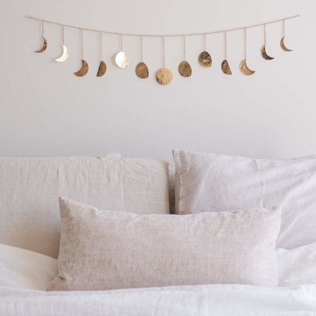 A gold garland draped above a bed, featuring moons in various waxing and waning phases strung along it