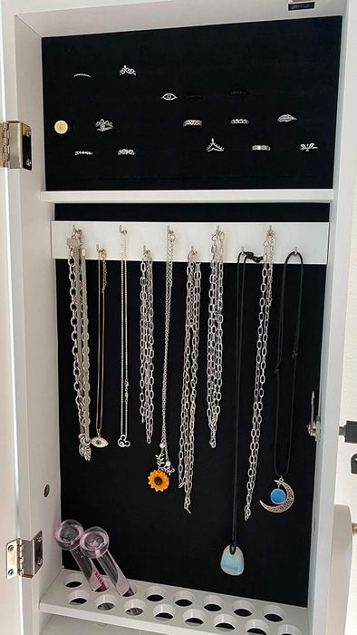 A jewelry organizer showcasing rings in the top section and hanging necklaces and chain bracelets below, with watches stored in the bottom compartment
