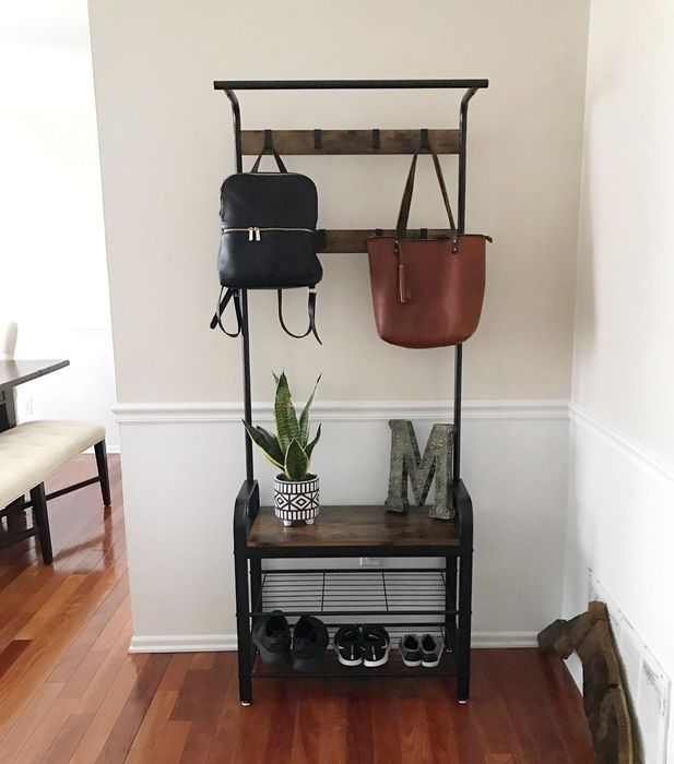a reviewer photo of their entryway organizer featuring shoes on the lower shelf, a few purses hanging from the hooks above, and a plant alongside a decorative letter M on the top shelf