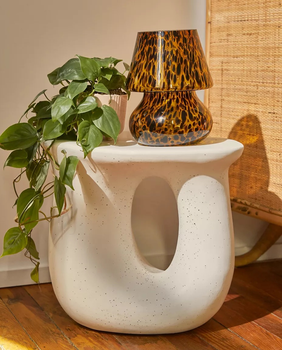The white table holding a small lamp and a plant.