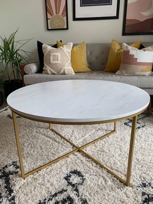 A reviewer's photo showcasing a round marble-top table with sleek gold legs.