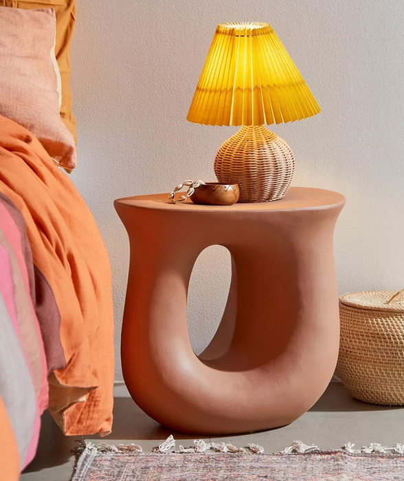 the rust-colored table positioned beside a bed, holding a lamp