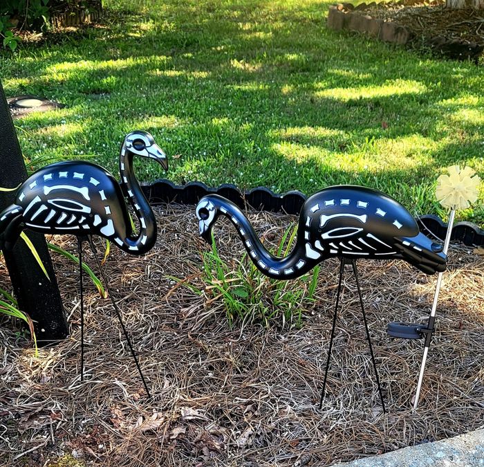 Two metal flamingo-shaped yard ornaments standing among grass and plants