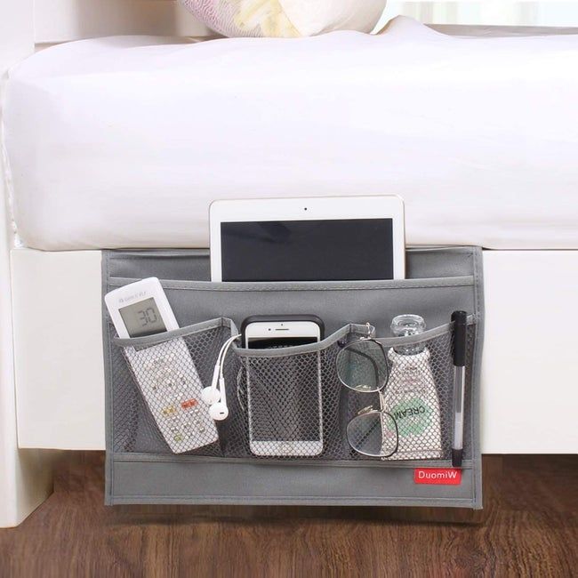 The grey bedside caddy holding items like a remote, iPad, cellphone, glasses, pen, lotion, and headphones