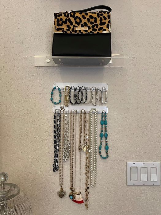 A wall-mounted jewelry organizer showcased by a reviewer, featuring an array of necklaces neatly hung and a leopard-print clutch placed on the top shelf.