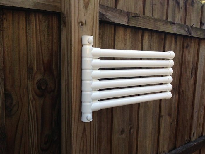 A white, wall-mounted towel rack with five bars, attached to a wooden fence