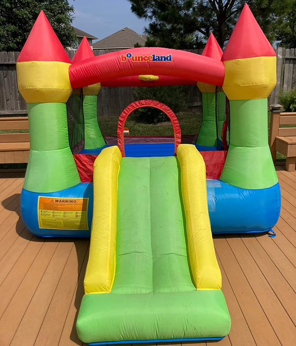 An inflatable bounce house with a slide by Bounceland, placed on a wooden deck in a backyard