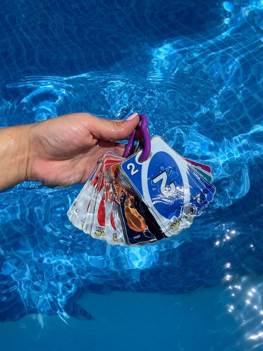 A hand dipping a deck of cards into a pool