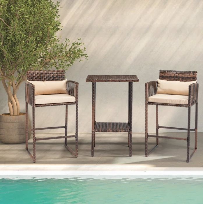 A stylish outdoor wicker bar set complete with two chairs and a table, positioned next to a pool with a potted plant adding a touch of greenery.