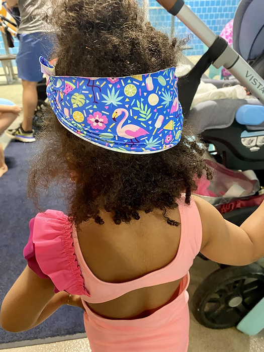 A child wearing a floral visor and a pink swimsuit with ruffles, seen from behind