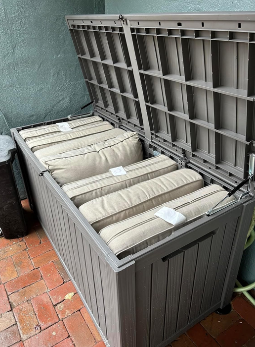 An outdoor storage bench containing beige cushions inside