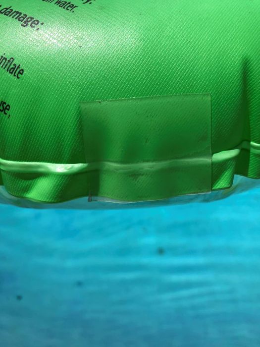 A close-up of a green inflatable pool float partially submerged in water, with visible text on it