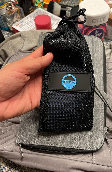 A hand holds a black mesh bag with a label clearly visible.