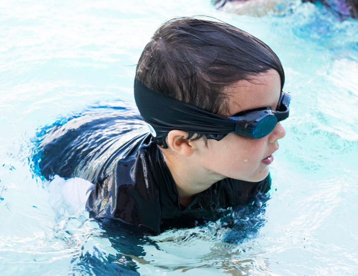 A reviewer's child in a pool, wearing black goggles with a fabric strap