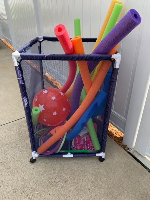 A blue mesh organizer holding pool noodles and other toys