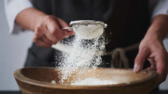 A woman sifting flour through a fine mesh sieve