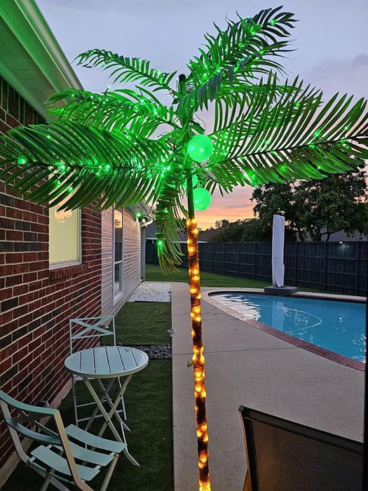 A lit-up palm tree standing proudly near patio furniture and a pool, creating a relaxing tropical atmosphere.