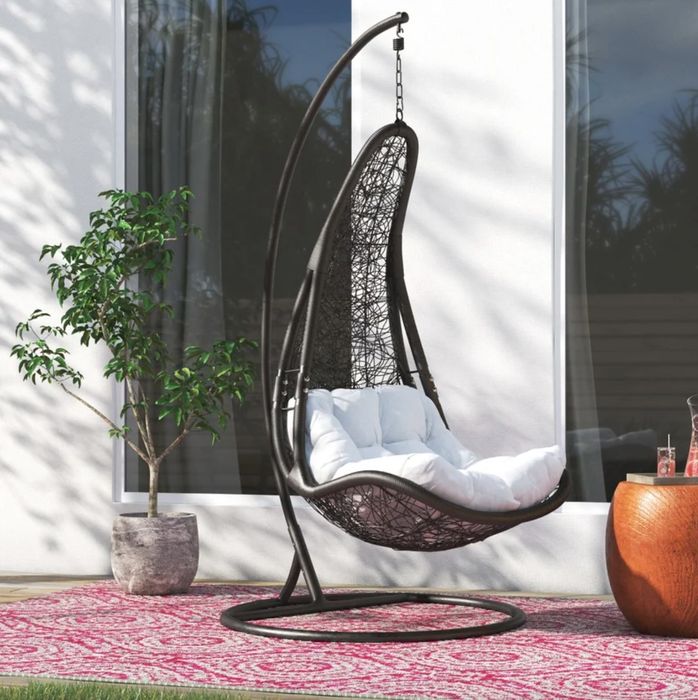 A grey swing chair with a white cushion, nestled in a beautifully decorated outdoor space.