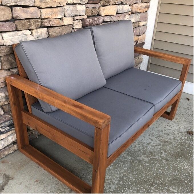 A wood-framed outdoor loveseat with soft grey cushions, ready for relaxation.