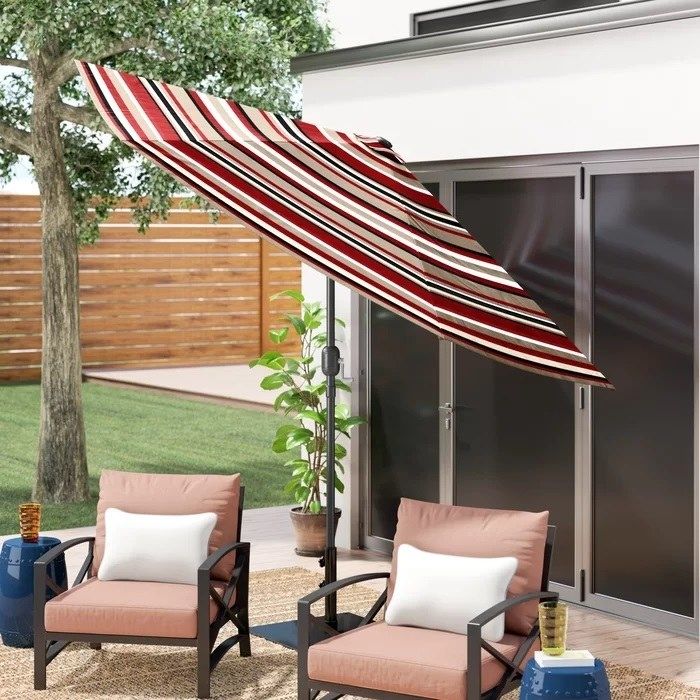 A striped tilting umbrella providing shade over two comfortable patio chairs.