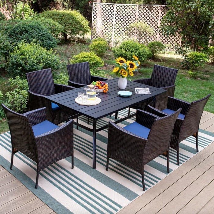 A large black metal table surrounded by six black chairs with blue cushions, set in a beautifully decorated outdoor space.