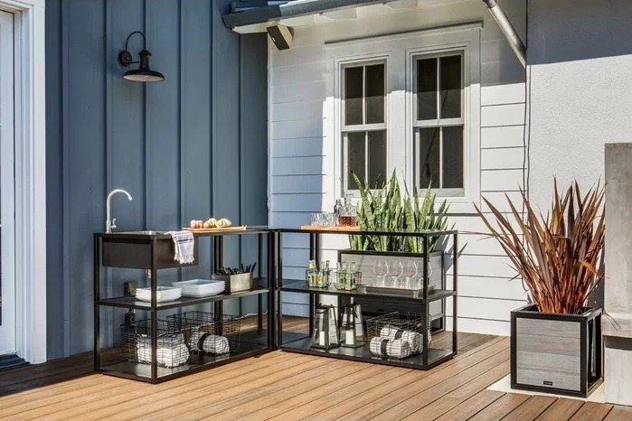A set of metal kitchen shelves with a sink placed on a patio, creating a functional outdoor cooking space.