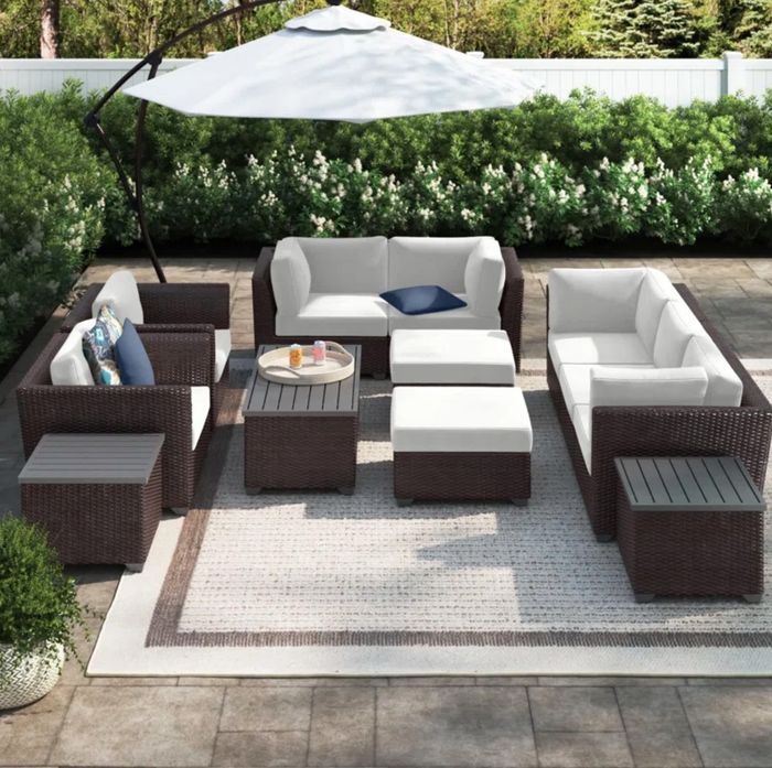 A dark wood furniture set with light cushions, placed on a soft outdoor rug with a matching umbrella, creating a serene outdoor space.