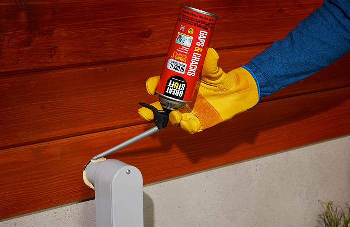 A model's hand applying foam sealant around a gap