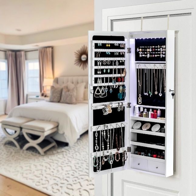 Wall-mounted organizer displaying jewelry and cosmetics, including earrings, necklaces, and makeup in an elegant bedroom setting