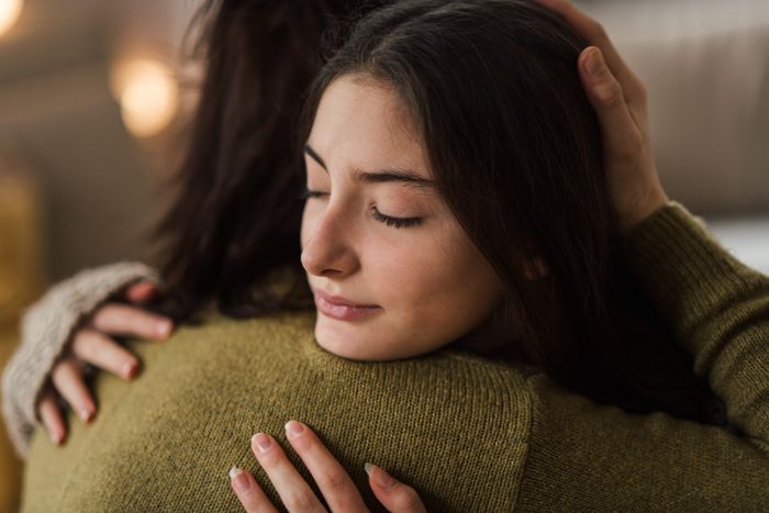 Two individuals embracing one another, with one looking away and the other with eyes closed, symbolizing warmth and connection